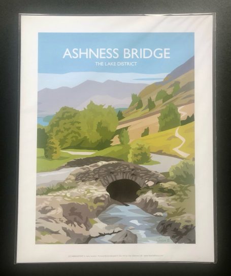 A scenic view of Ashness Bridge surrounded by hills and greenery.